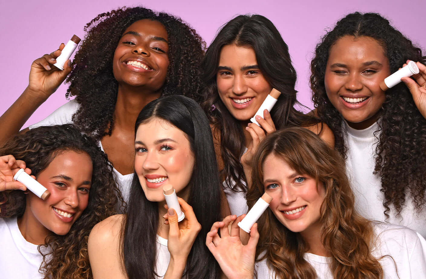 Groupe de femmes aux textures de cheveux variées tenant un produit cosmétique sur fond rose .